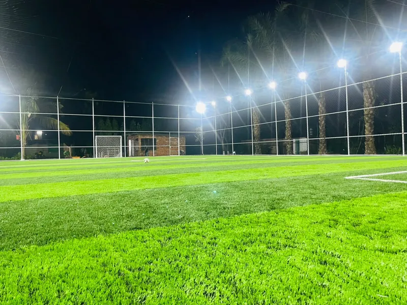 Floodlit pitch at night with a ball near the far goal